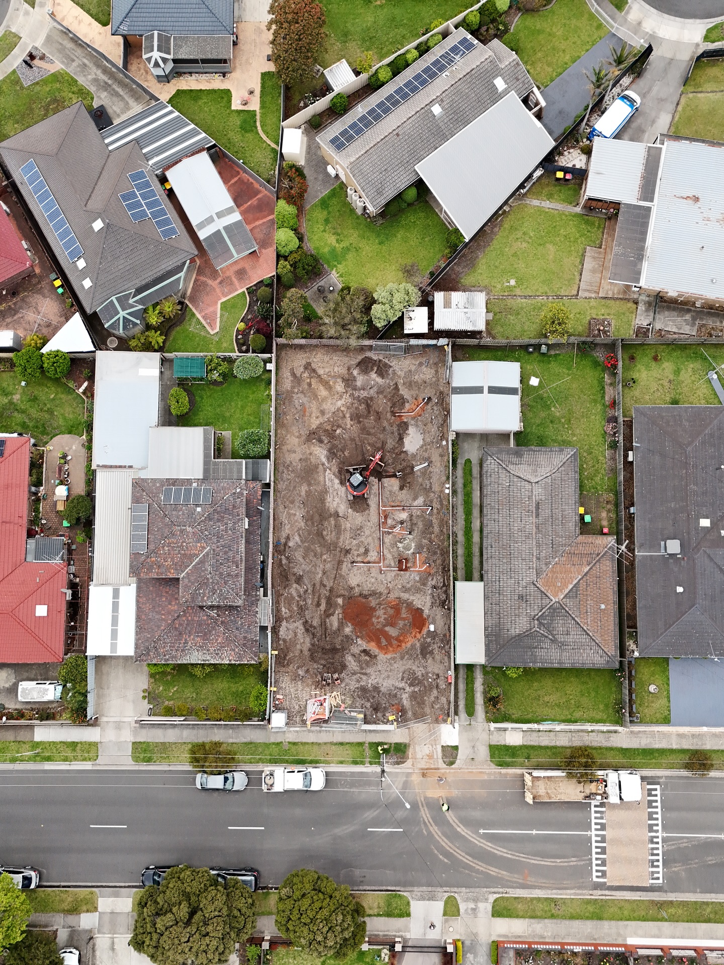 Drone view of a suburban block stripped to subgrade, with the drainage layout pegged out on the soil.