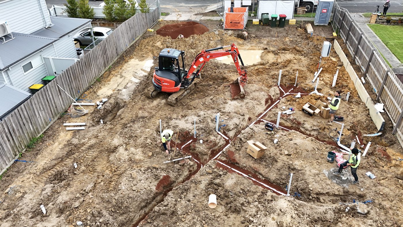Open excavation on a residential site with drainage pipe laid out in the trench.