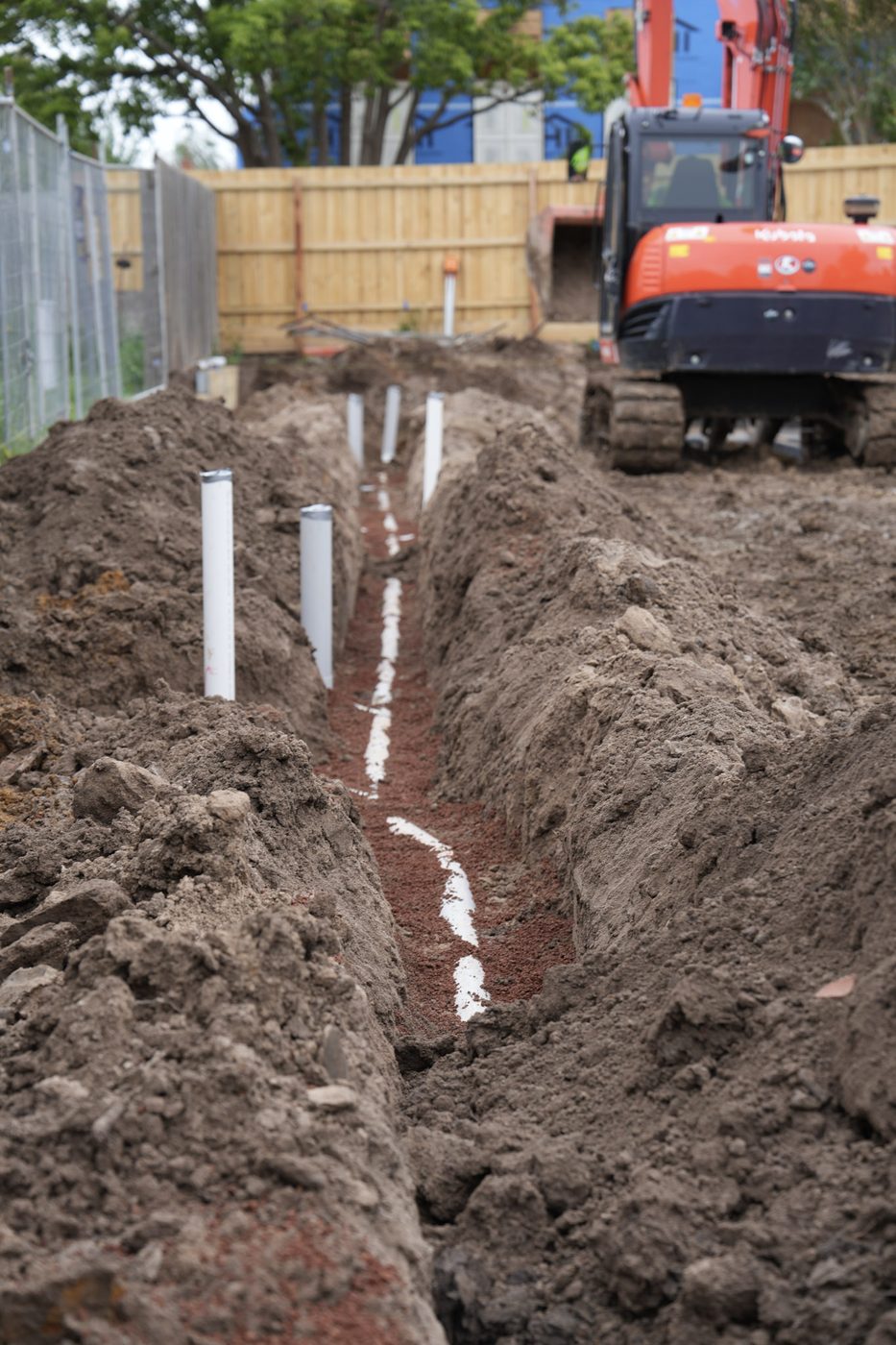 Excavator trenching out for a new drainage run with orange pipe alongside.